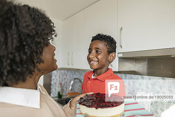 Happy mother and son with cake in kitchen at home