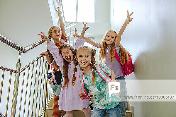 Smiling schoolgirls with hand raised standing on school staircase