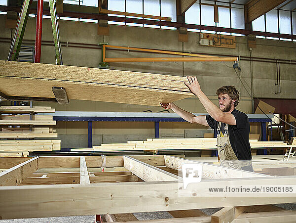 Carpenter holding oriented strand boards on crane in workshop