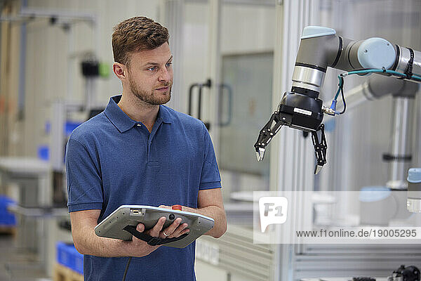 Technician operating robotic arm using equipment in industry
