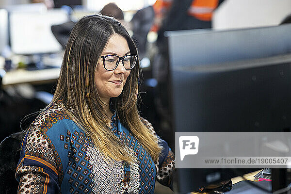 Smiling businesswoman wearing eyeglasses working on computer in office