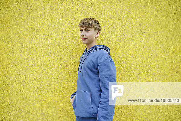 Thoughtful boy standing in front of yellow wall