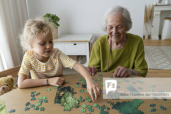 Smiling grandmother and granddaughter solving jigsaw puzzle