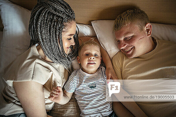 Parents and son lying on bed at home