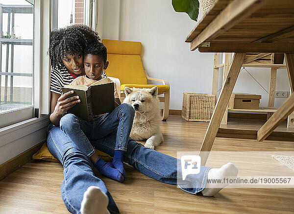 Mother and son reading book and sitting by dog at home