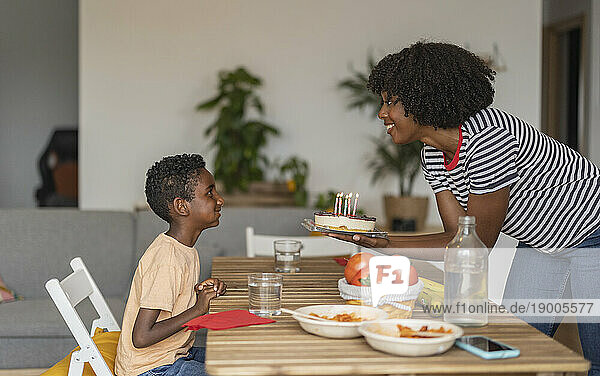 Happy boy with mother holding birthday cake at dining table
