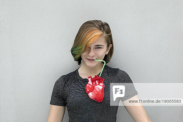 Teenage girl drinking from heart against gray background