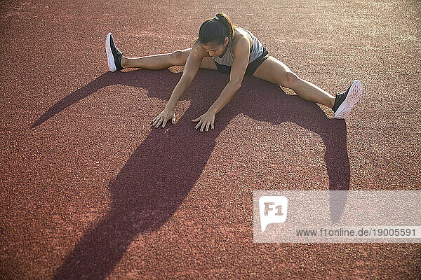 Young woman doing stretching exercise in sports field