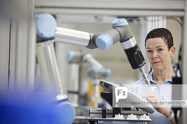 Mature technician testing robotic arm using equipment in industry