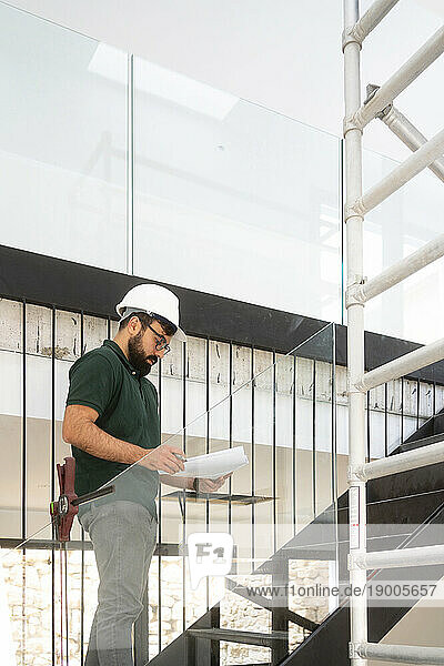 Architect with document standing on staircase at construction site