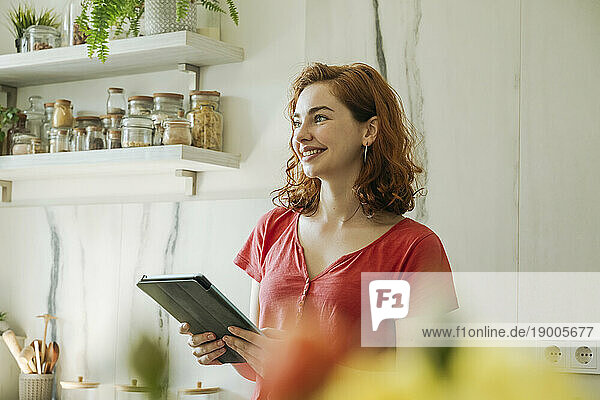 Smiling young woman standing with tablet PC in kitchen at home