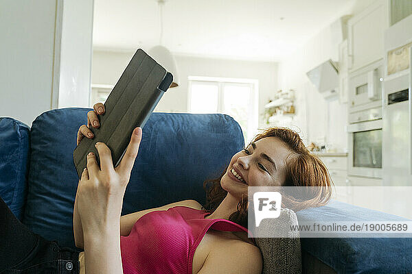 Happy young woman relaxing and using tablet PC at home