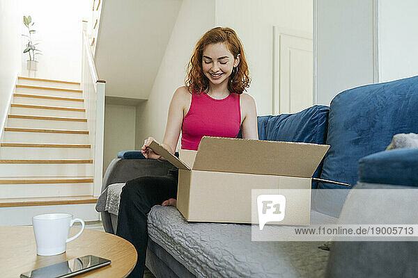 Happy young woman unboxing package on sofa at home