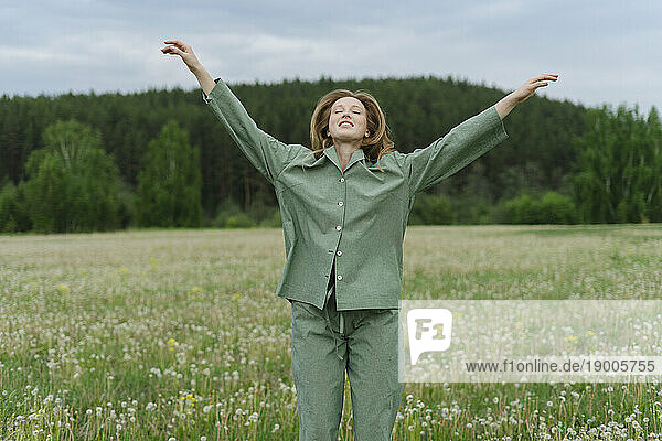 Carefree young woman with arms raised on dandelion field
