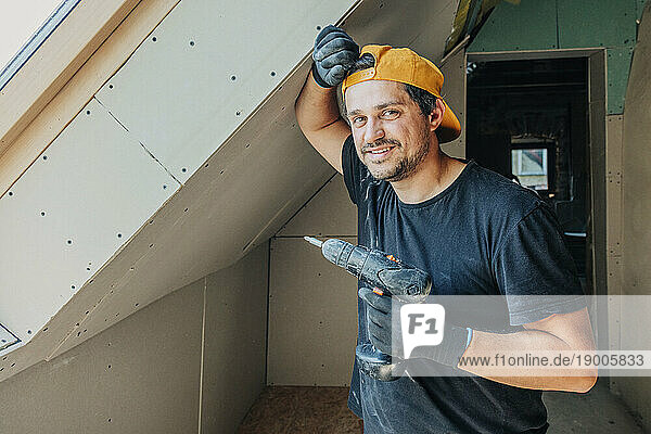 Smiling man holding drill in attic