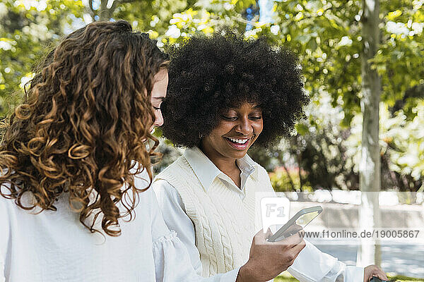 Happy woman using smart phone with friend in park