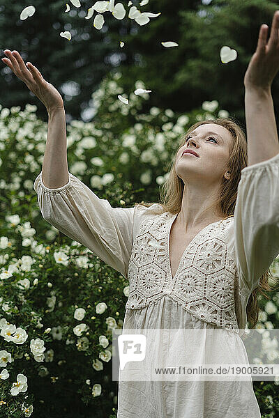 Young woman throwing petals by white flower bush