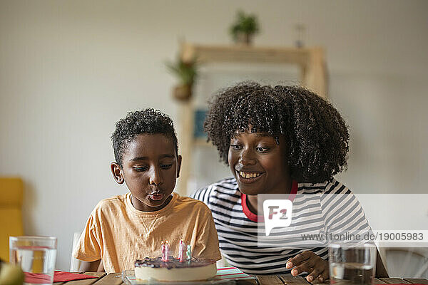 Happy mother with son blowing candles on cake at home