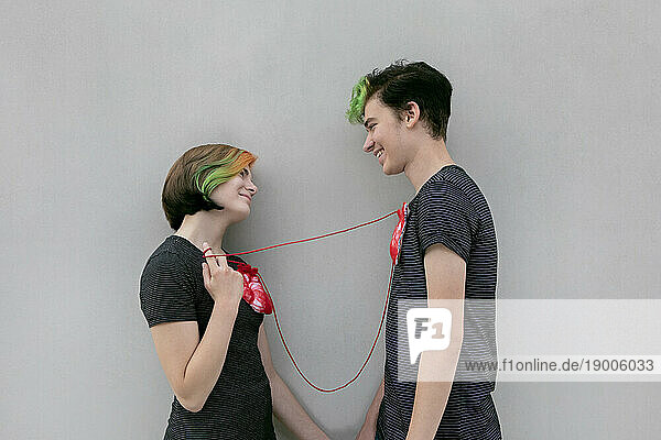Teenage couple connected hearts with rope against gray background