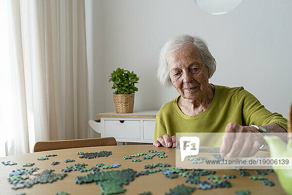 Elderly woman solving jigsaw puzzle on table