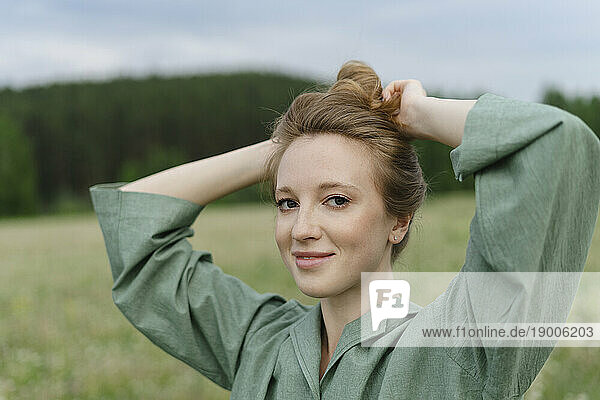 Smiling young woman tying hair bun on field
