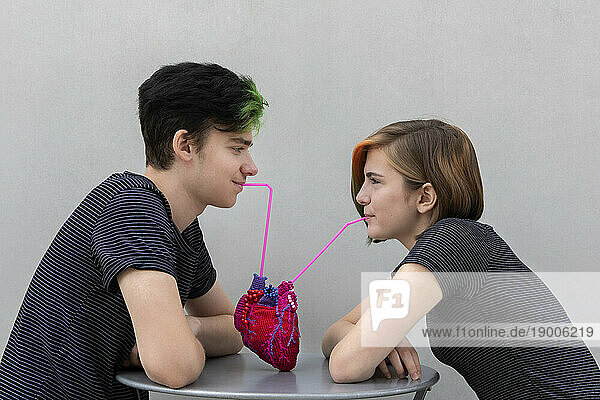 Teenage couple drinking from model heart against gray background