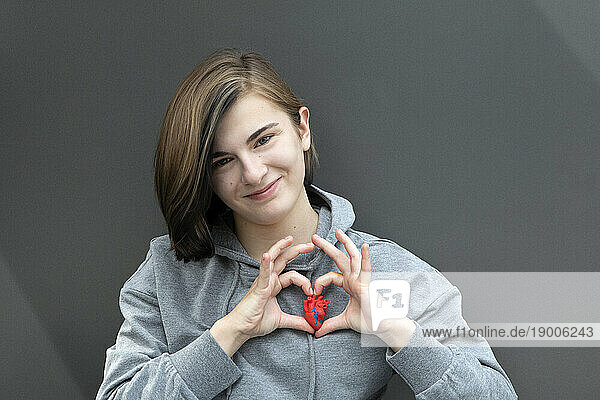 Teenage girl gesturing with model heart against gray background