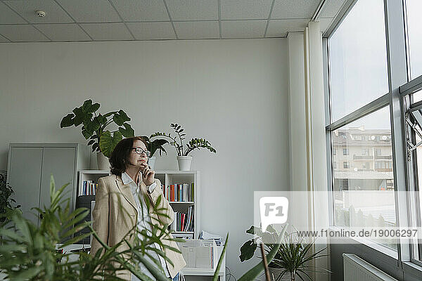 Thoughtful senior businesswoman looking through glass window in office