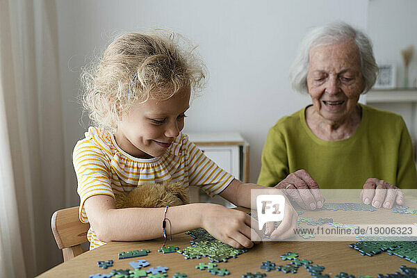 Granddaughter and grandmother solving jigsaw puzzle on table