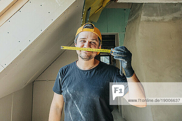 Happy man holding measuring tape in attic