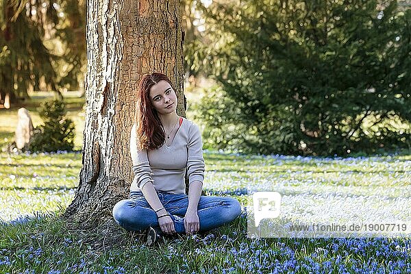 Verträumte junge Frau sitzt auf einer Blumenwiese