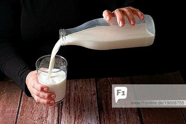 Hände einer Frau  die frische Milch in ein Glas gießt  mit einer Glasflasche