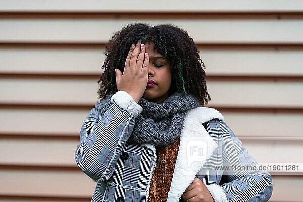 Schwarze ethnische Frau  die an einer grauen Wand eine Stop Rassismus Geste macht und dabei ihre Augen bedeckt