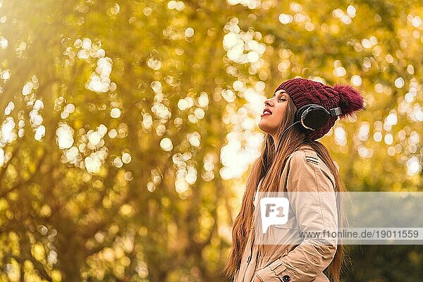Porträt einer Frau im Herbst in einem Wald mit braunen Blättern  mit geschlossenen Augen  die mit Kopfhörern Musik hört