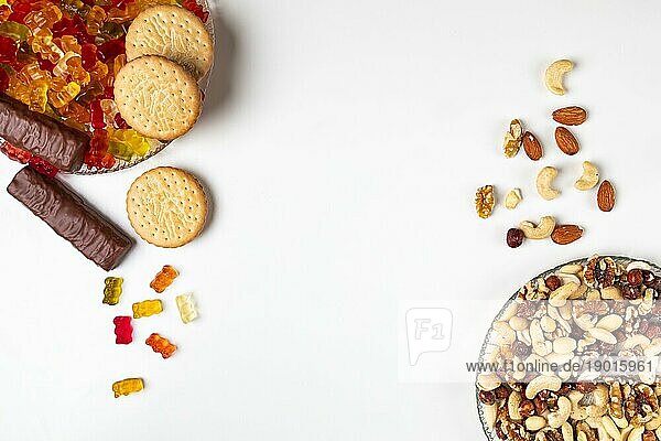 Gegenüberstellung ungesund und gesund  verschiedene Süßigkeiten und Nüsse  auf Tellern  weißer Hintergrund  Kopierraum