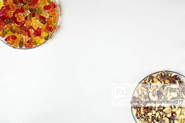 Gegenüberstellung ungesund und gesund  Gummibärchen und verschiedene Nüsse  auf Tellern  weißer Hintergrund  Kopierraum