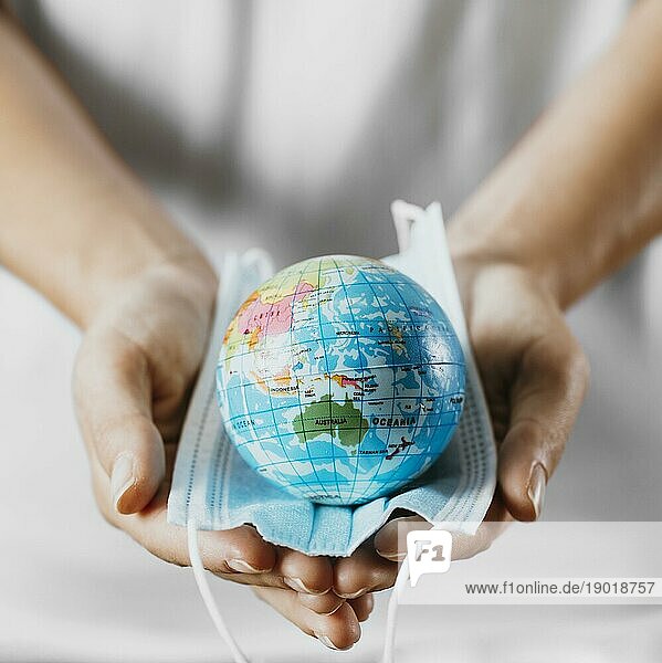 Hohe Winkel Person hält medizinische Maske mit Erde Globus. Foto mit hoher Auflösung
