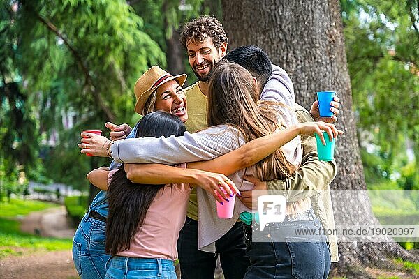Multiethnische Gruppe der Geburtstagsfeier im Stadtpark umarmt in einem Symbol der Freundschaft für immer