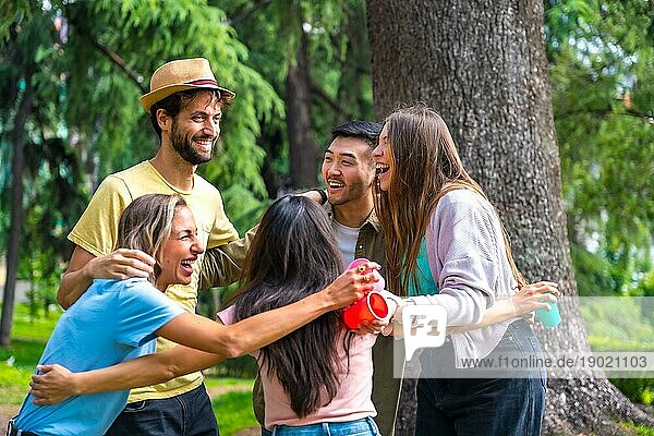 Multiethnische Gruppe von Geburtstagsfeier in der Stadt Park umarmt in einem Symbol der Freundschaft für immer und lächelnd eine Menge