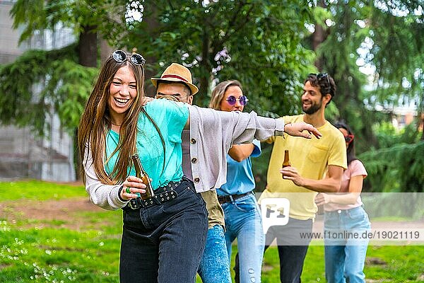 Eine Gruppe multiethnischer Freunde tanzt auf einer Geburtstagsfeier im Stadtpark  ein sommerlicher Spaß beim Conga Tanz
