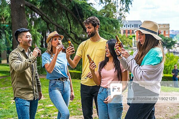Eine multiethnische Gruppe von Freunden feiert in einem Stadtpark mit Bier. Freunde trinken kaltes Bier