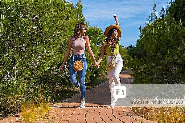 Weibliche Freunde haben Spaß im Urlaub in einem Park im Sommer zu Fuß und springen vor Freude auf einem Weg