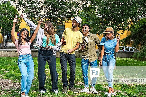 Eine multiethnische Gruppe von Freunden feiert in einem Stadtpark und hat Spaß mit Bierflaschen