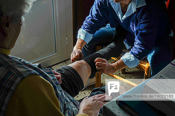 Freelance nurse during her daily visit to an elderly person. Leg care and placement of a compression sock.