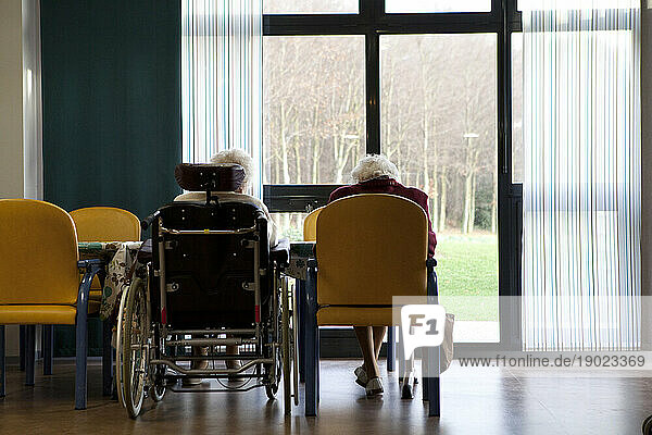 Two elderly people in a retirement home in front of a window.