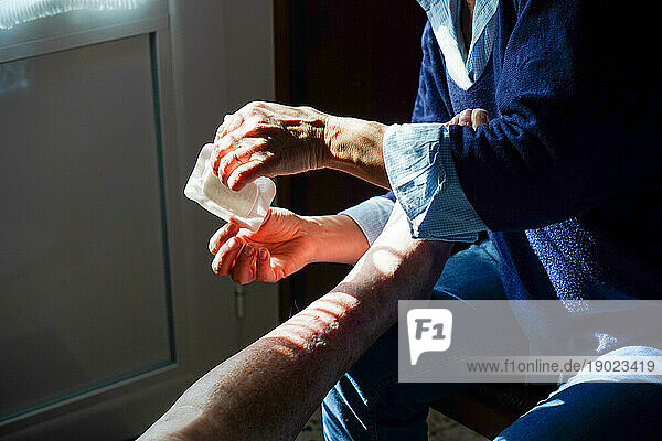Freelance nurse during her daily visit to an elderly person. Leg care and placing a bandage on a wound.
