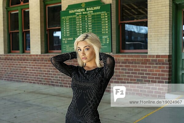 Ein wunderschönes junges blondes Modell posiert im Freien  während es auf einen Zug in einem Zugdepot wartet