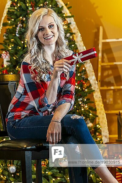 Ein wunderschönes blondes Model genießt die Feiertage zu Hause mit einem Weihnachtsbaum und Geschenken