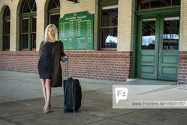 Ein wunderschönes junges blondes Modell posiert im Freien  während es auf einen Zug in einem Zugdepot wartet