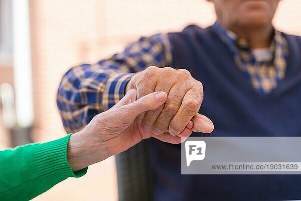 Detail der Hände zweier älterer Menschen im Garten eines Pflegeheims oder Seniorenheims  die sich in einem Moment der Zuneigung an den Händen halten